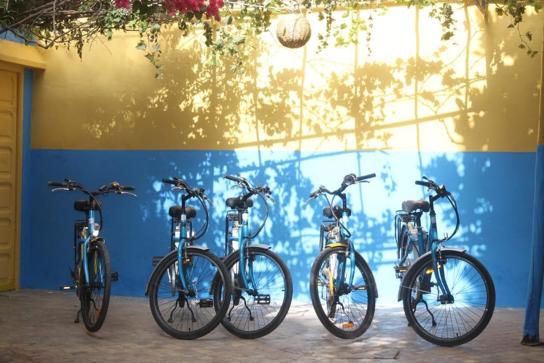 Cinque bici allineate davanti a un muro blu e giallo illuminato dal sole