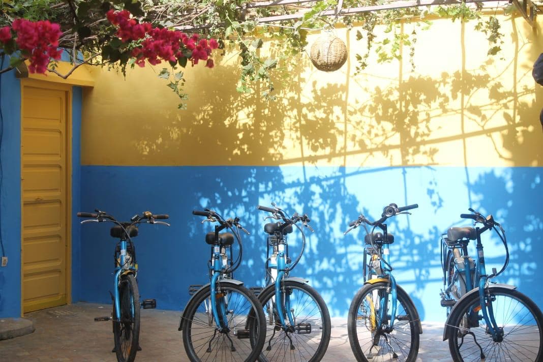 Vélos Yellow Bike garés dans une cour bleue et jaune, sous les bougainvilliers